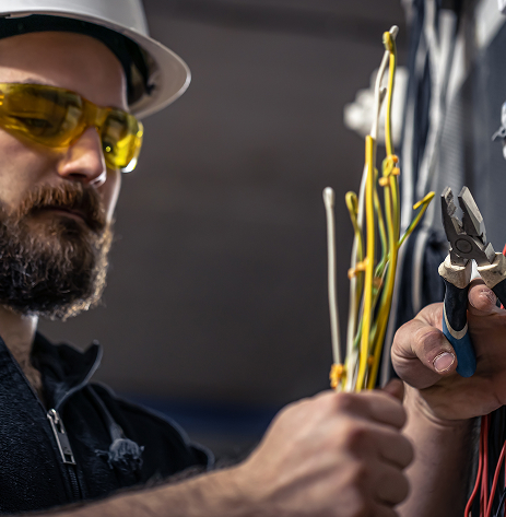 Électricien coupe fils dans un panneau électrique.
