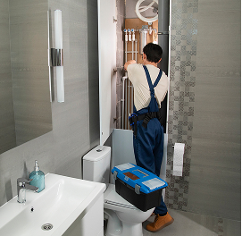 Plombier répare plomberie dans salle de bains moderne.