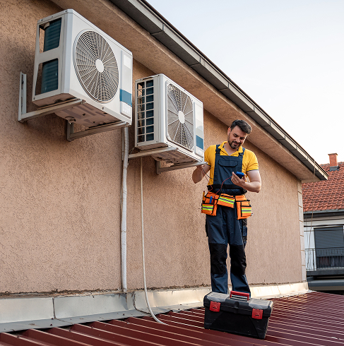 Technicien réparant des climatiseurs sur un toit.