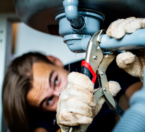 Plombier réparant tuyau sous évier avec clé.